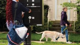 Letter carrier Latasha Thompson services mailboxes as a dog passes by.